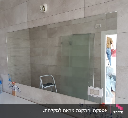 מראה גדולה על קיר עם זכוכית מקלחת